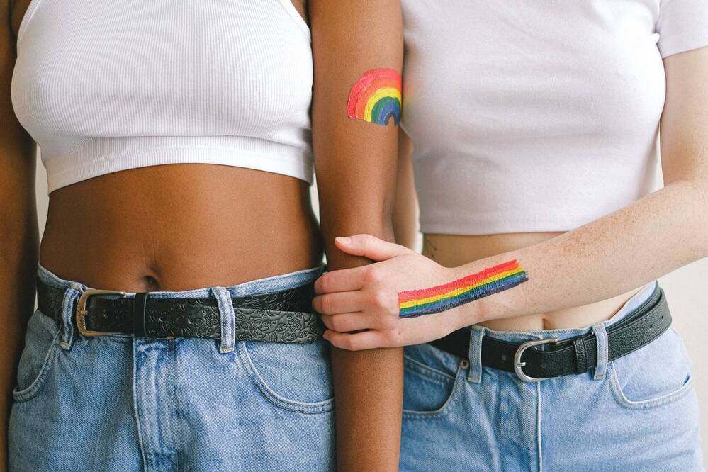 duas meninas com símbolos da bandeira LGBTQIAP+ nos braços